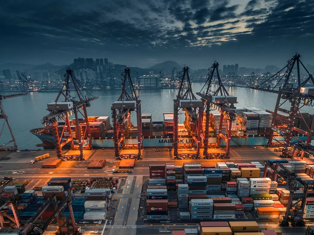 Terminal à conteneurs éclairé à la tombée de la nuit, grues et piles de conteneurs